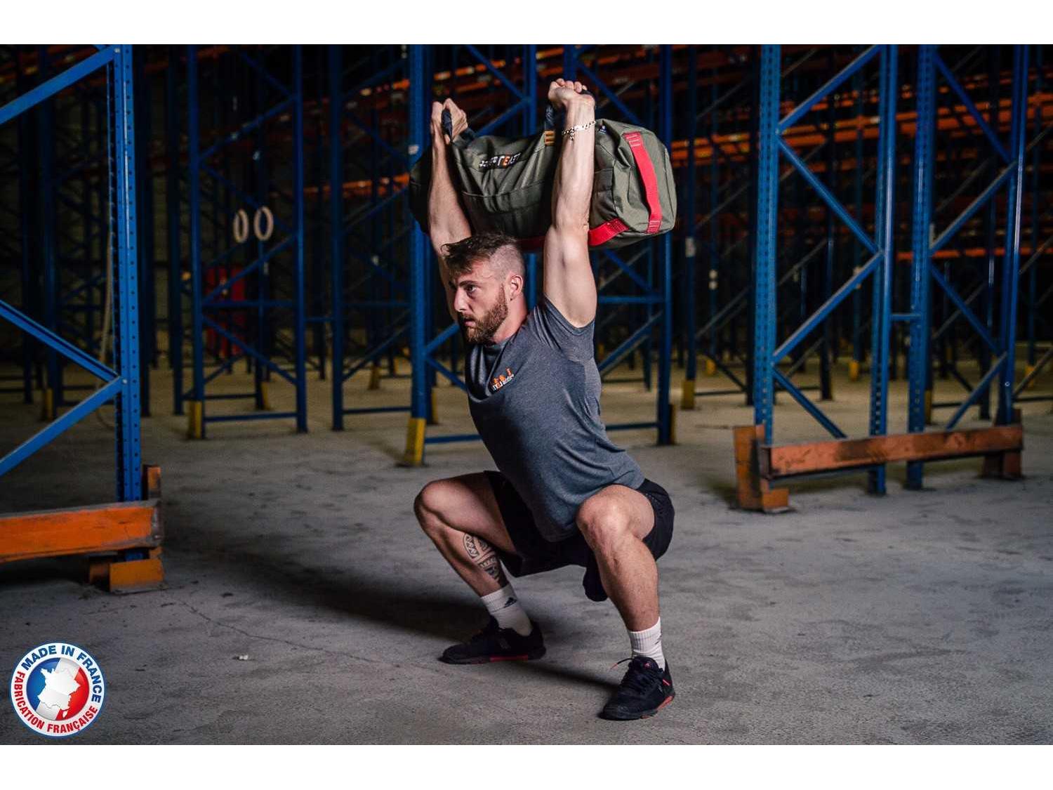 Homme en position overhead squat avec sandbag L - LEVEL addict Homme en position overhead squat avec sandbag L - LEVEL addict